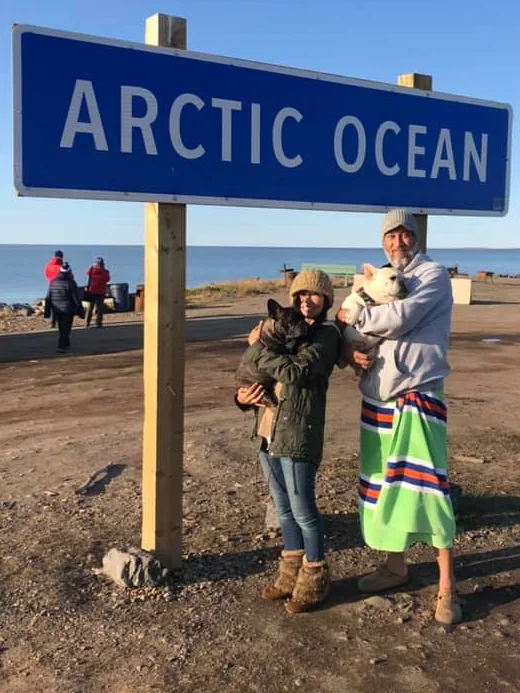 Tony and Hiroko holding Matsu and Porco under the Arctic Ocean sign in Tuktoyaktuk